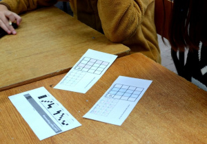 Na stoliku leżą karty pracy z tabelkami do kodowania rysunków.